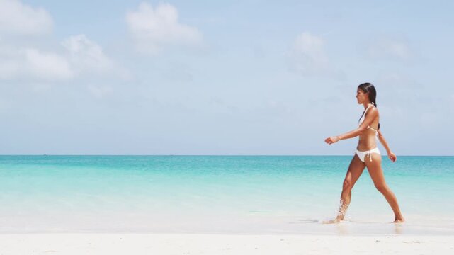 Beautiful woman in white bikini walking at beach. Young female enjoying summer travel vacation. Video of real unretouched woman model without any makeup