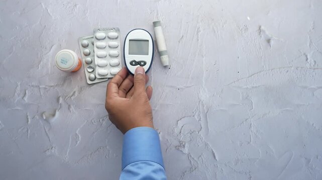 Hand picks up glucose meter and diabetes medication on white textured surface motion