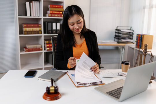 Young asian woman lawyer or attorney reviewing legal contracts and documents on her desk with justice scales and a gavel, working on legal consultation in a modern office