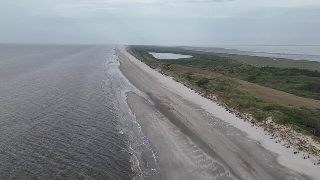 Elevated drone shot follows beach waterline with lake and village in background.