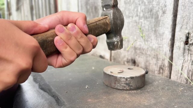 Detailed close up shot of a person using a vintage ball-peen hammer to strike a small metal part. Ideal for industrial, hardware, craftsmanship, and DIY tutorial videos.