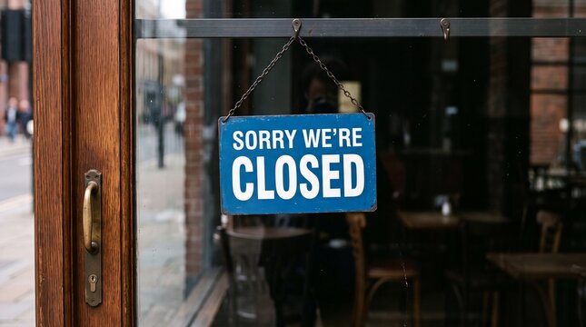 A blue sign reading Sorry We&rsquo;re Closed hanging on a rustic wooden storefront door of a cafe or restaurant.