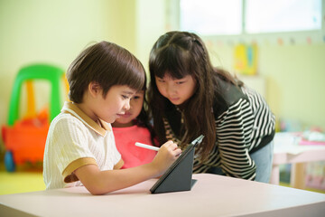 Obraz premium Young children collaborate around a digital tablet in a bright classroom, developing creativity, teamwork, and early technology skills through interactive learning.