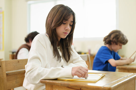 Focused schoolgirl completes an exam in a classroom while classmates work independently, representing academic assessment, concentration, and a positive educational environment.