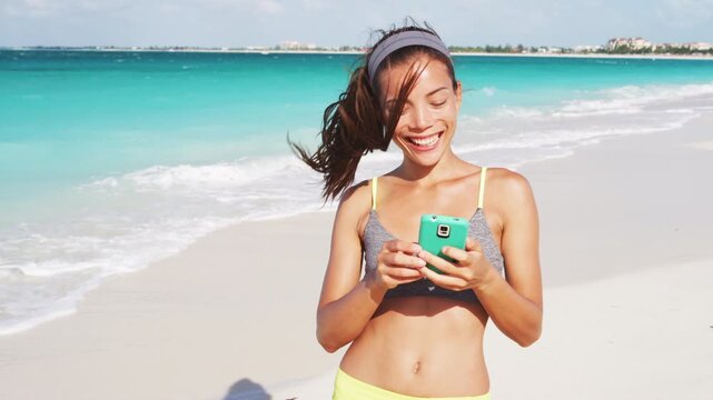 Woman with phone standing on beautiful exotic beach. unrecognizable fitness girl using phone. Video is unretouched and model without makeup. Raw footage.