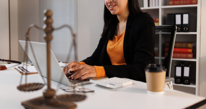 Female lawyer working on laptop, preparing legal documents in office with scales of justice and law books, delivering expertise and professional counsel