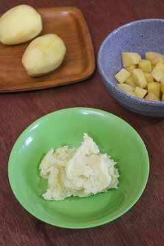 Mashed potatoes in green bowl with diced and whole peeled potatoes background