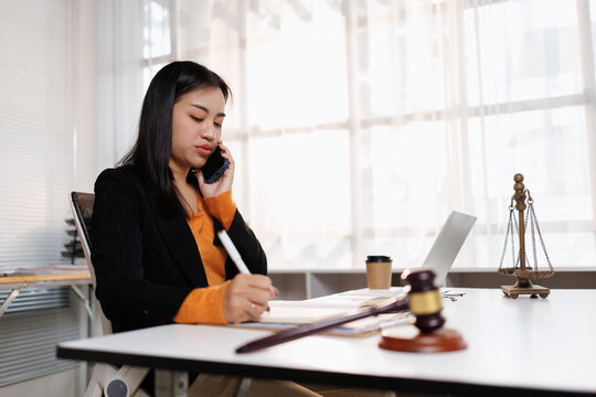 Young asian woman working at a modern office desk. Actively engaging in a phone conversation while simultaneously jotting down important information