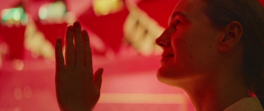 Person with raised hand gazing upward in warm red ambient light indoors