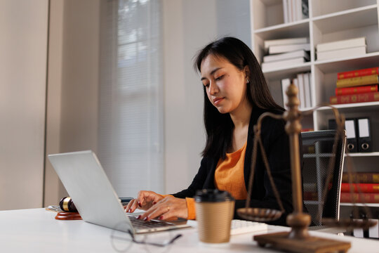Woman lawyer or attorney working on her laptop at a desk in a legal office. Surrounded by symbols of justice like scales and a gavel. Focusing on legal research. Case management