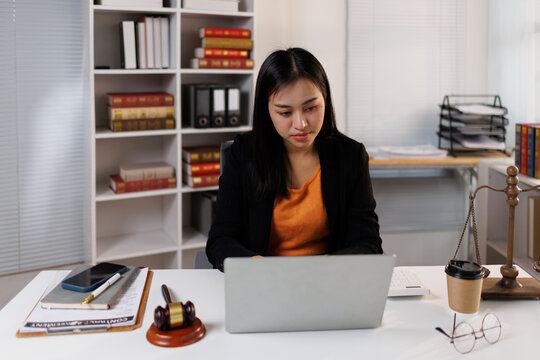 Asian woman lawyer working on laptop in law office, preparing legal documents and case files, symbolizing professional female legal expertise and justice in a modern diverse workplace