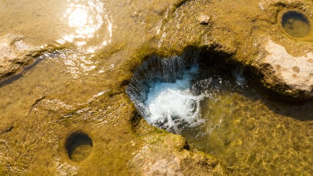 Aerial view of a natural rock pool with flowing water and surrounding moss-covered stones