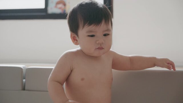 Cute Asian baby boy playing with busy board toy at home, early childhood development.