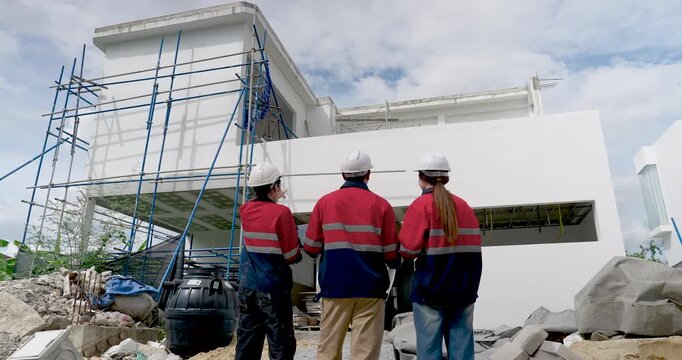 Asian woman engineer and male supervisor inspect exterior wall section near scaffold, coordinating construction quality control, safety compliance, building progress meeting outside project site