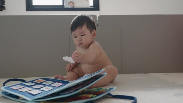 Cute Asian baby boy playing with busy board toy at home, early childhood development.