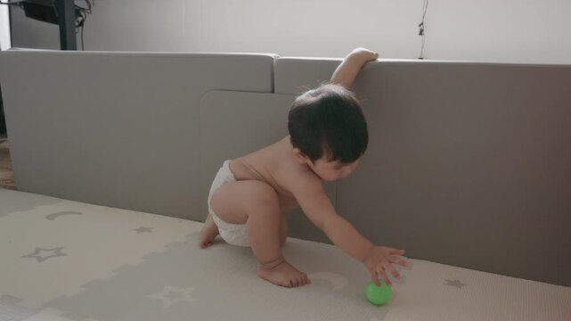 Cute Asian baby boy playing with busy board toy at home, early childhood development.