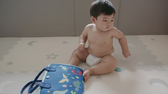 Cute Asian baby boy playing with busy board toy at home, early childhood development.