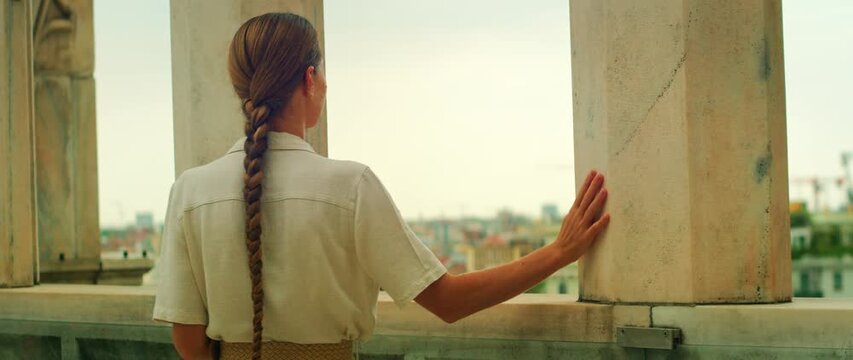 Woman touching stone pillar and overlooking Milan city at Duomo rooftop in Italy