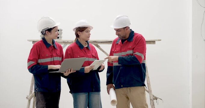 Female Asian engineer uses laptop during construction document review, woman inspector studies report, male contractor compares blueprint for workplace safety and building project planning work.