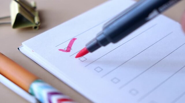 Person marking to do list with red felt pen on white notepad