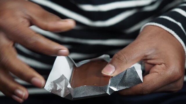 Person unwrapping chocolate bar with hands in slow motion