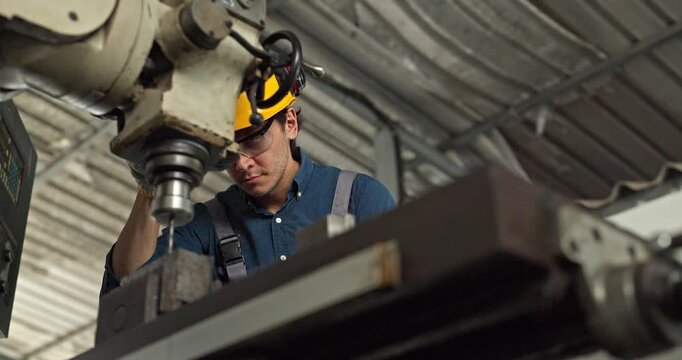 Factory worker operating industrial drilling machine to machine metal part in workshop