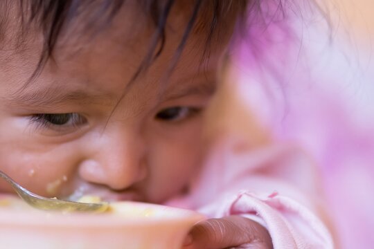 Extreme close up of a messy baby eating from a spoon for childcare and nutrition themes, showing natural food on the face and a nurturing home mood