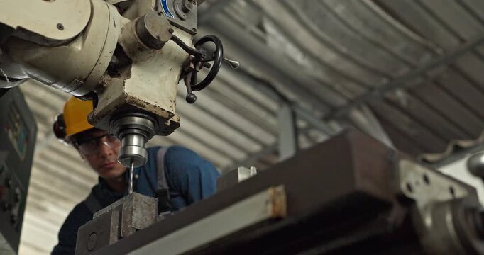 Factory worker operating industrial drilling machine to machine metal part in workshop
