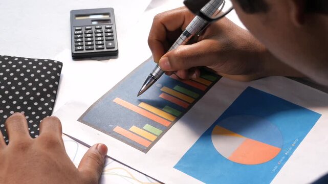 Close up of person reviewing financial charts with calculator and pen