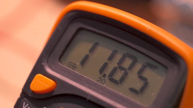 Close up of a digital measuring device with an LCD display showing changing readings. Orange handheld instrument with shallow depth of field and selective focus