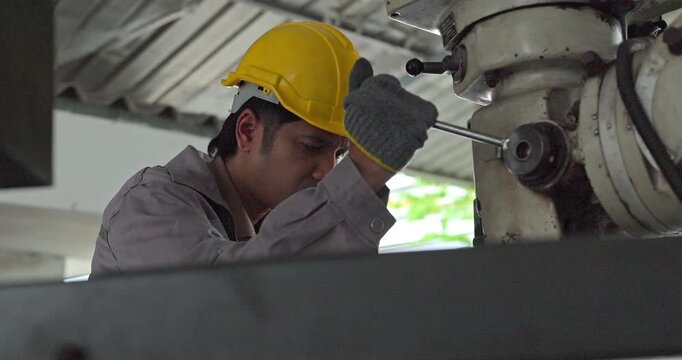 Factory worker operating industrial drilling machine to machine metal part in workshop