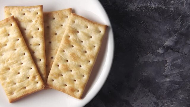 Close up motion footage of plain crackers stacked on white plate, healthy snack on dark textured background