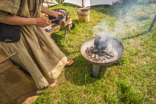 Person in historical clothing cooking over an open fire with a cast iron pot