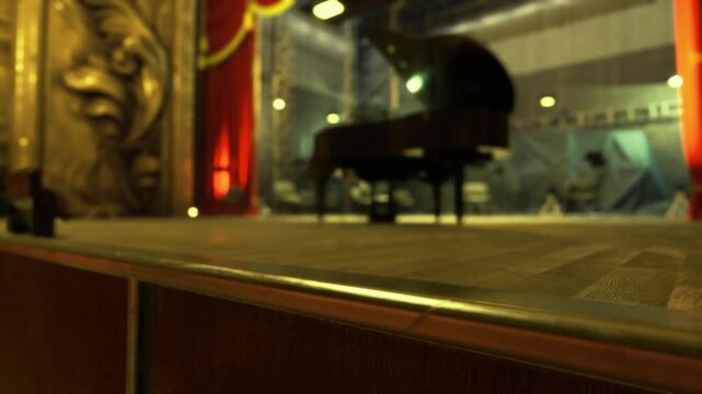 Empty concert stage grand piano center, warm golden lighting, shallow depth of field, polished wood foreground, distant audience blur, backstage curtain