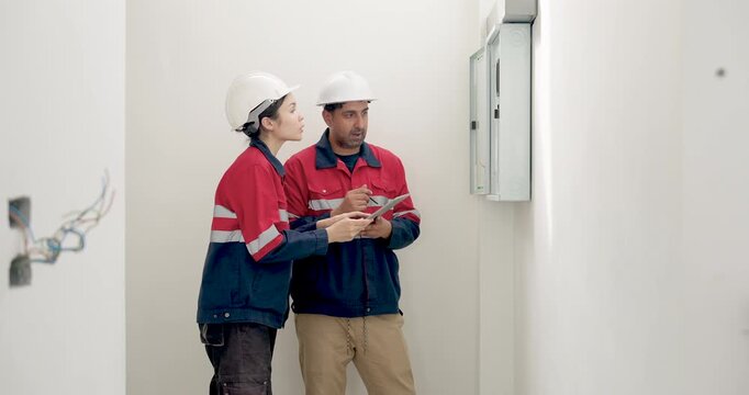 Asian female engineer checks clipboard beside male manager during indoor building inspection, discussing construction report, project progress, safety planning, and quality control work today.