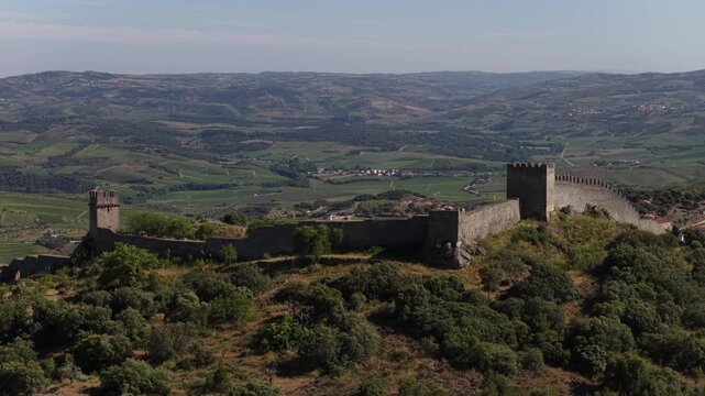 Aerial footage of Numao Castle atop a lush hill, surrounded by rolling valleys and rustic Portuguese countryside under clear daylight skies.