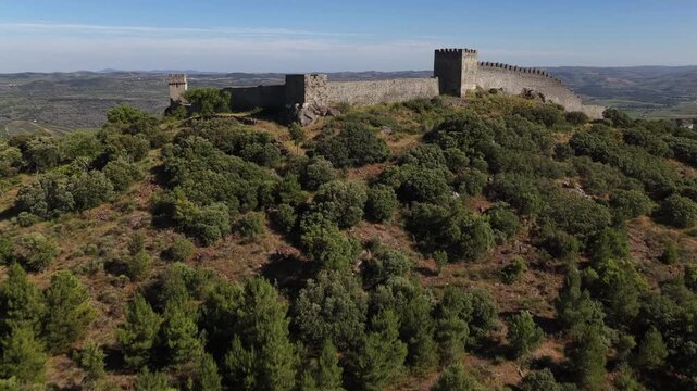 Stunning drone video showcases Numao Castle atop a verdant hill, surrounded by forested slopes and rural scenery under clear blue skies. Wide angle aerial footage captures historic architecture.
