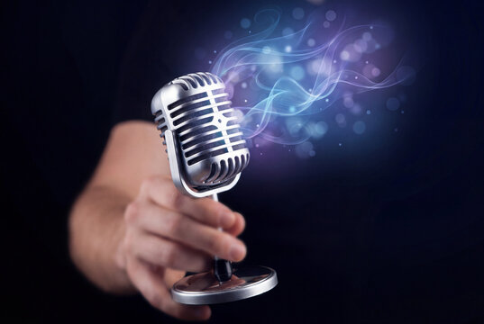 Hand holding a vintage silver microphone in dark blue light