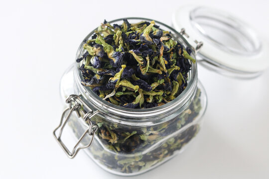 Dried butterfly pea flowers stored in a clear glass jar, isolated on a white background.