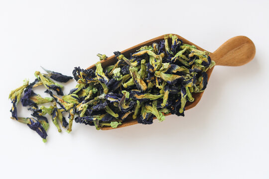 A wooden scoop of dried butterfly pea flowers, isolated on a white background.