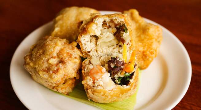 A plate of crispy stuffed tofu, also known as tahu kipas in Indonesia with one of the tofu sliced in half to show the filling inside.