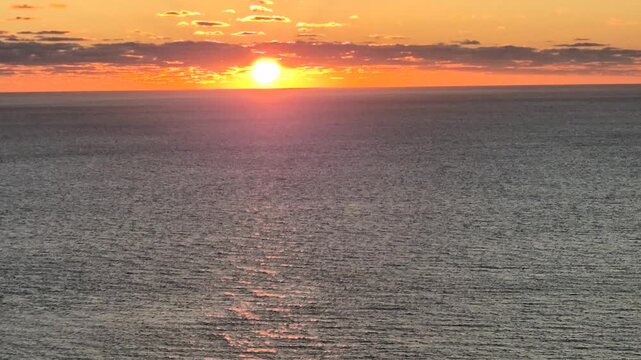 Ocean sunset reflection glows on dark rippling water as the golden sun dips below the horizon. Vertical panning shot.