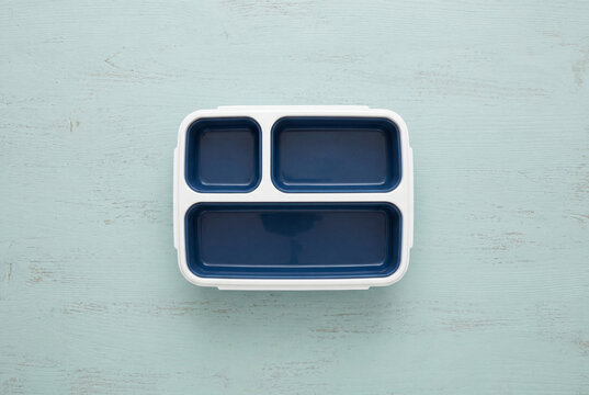 Empty blue and white plastic bento lunchbox flat lay on a light blue wooden surface background