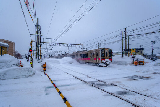 吹雪の中、踏切を駆け抜ける電車