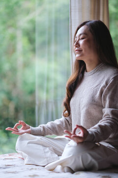 Vertical portrait image of a woman with closed eyes meditating or practicing yoga in lotus pose