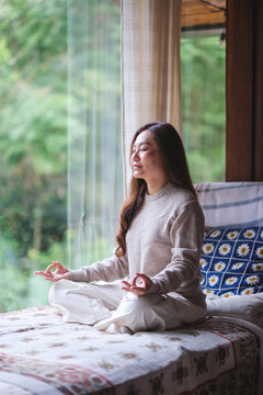 Vertical portrait image of a woman with closed eyes meditating or practicing yoga in lotus pose