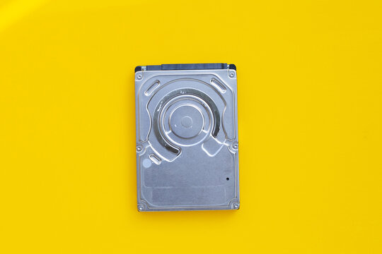 Top view of a metallic internal computer hard drive isolated on a bright yellow background.