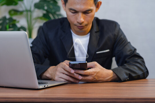 Businessman Using Smartphone at Desk with Laptop in Modern Office Setting