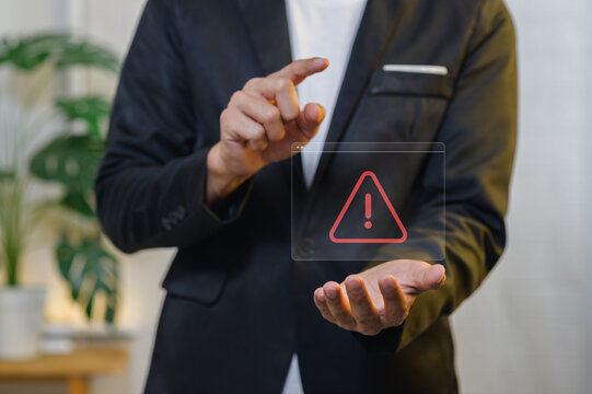 Businessman in suit pointing at digital warning alert on transparent holographic screen