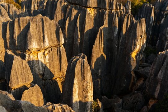 Rugged limestone formations bathed in golden sunlight, creating dramatic shadows and textures in a natural rock landscape.